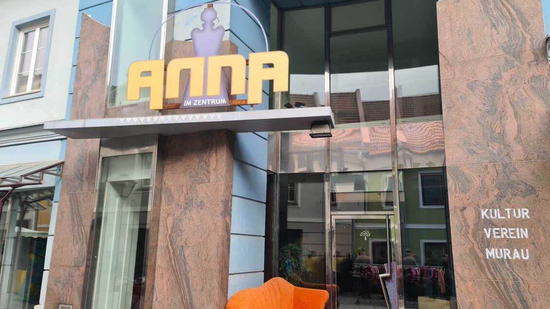 Ein modernes Gebäude mit großen Fenstern und einem auffälligen Schild mit dem Namen "ANNA". Vor dem Eingang befindet sich ein orangefarbenes Sofa. | © Tv Murau