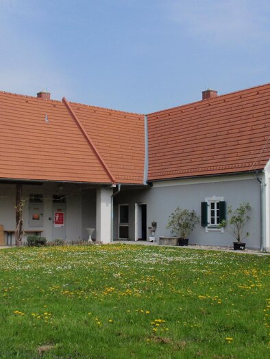Ein modernes Haus mit einem rotem Dach und weißen Wänden. Der Garten ist grün und blühend, mit vielen Löwenzahnblumen. | © Pavelhaus
