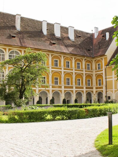 Ein historisches Gebäude mit gelber Fassade und großen Fenstern. Im Vordergrund befinden sich ein gepflegter Garten und ein gepflasterter Weg. | © TV Südsteiermark - Irene Löschnig