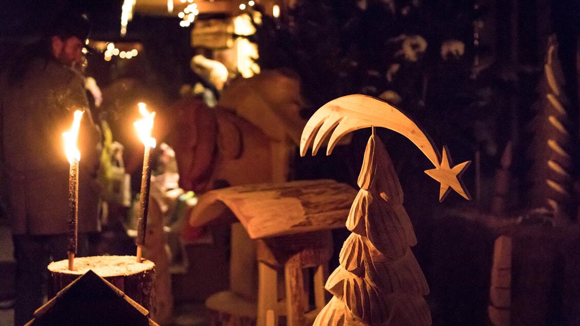 Eine festliche Nacht mit beleuchteten Ständen und Holzkunstwerken. Im Vordergrund steht ein geschnitzter Weihnachtsbaum mit einem Stern. | © Naturpark Zirbitzkogel-Grebenzen, Mediadome