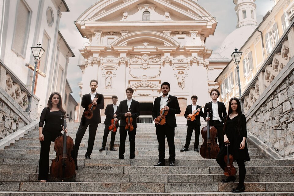 Das Oberton String Octet mit Violinen, Bratschen und Celli auf einer Freitreppe vor einer Kirche. | © Marija Jancic