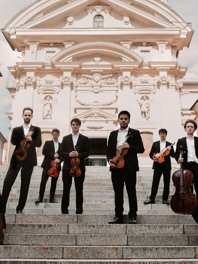 Das Oberton String Octet mit Violinen, Bratschen und Celli auf einer Freitreppe vor einer Kirche. | © Marija Jancic