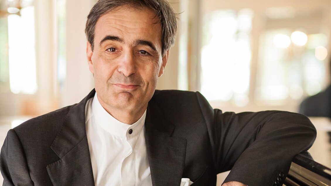 Porträt des Pianisten Paul Gulda im dunklen Anzug, an einen Flügel gelehnt. | © Julia Grandegger