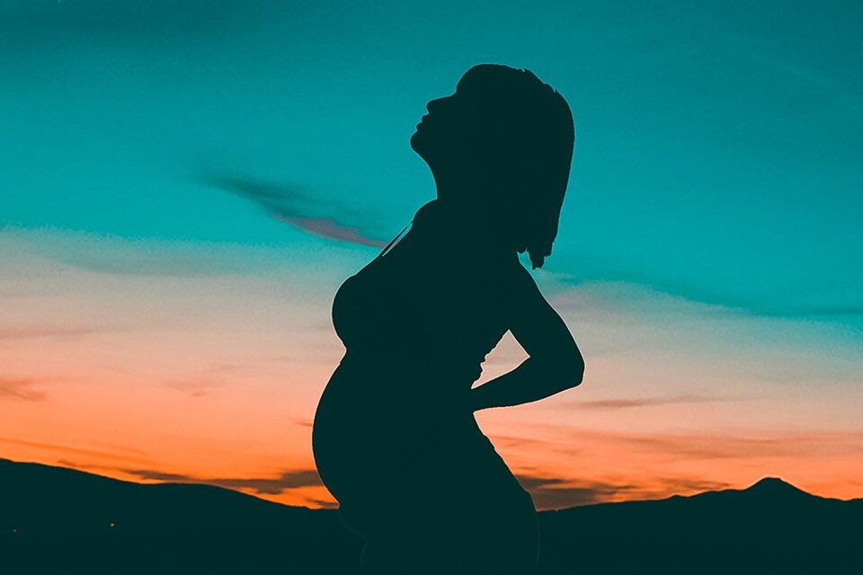 Eine schwangere Frau steht in Profilansicht vor einem bunten Sonnenuntergang. Die Silhouette betont ihre Rundung und die sanften Farben des Himmels. | © Bild: Pexels