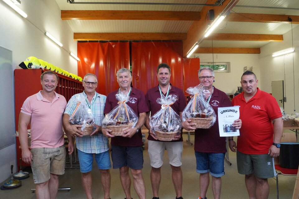 Siegerehrung eines Stockturniers in Gruisla: Gruppe von sechs Männern in Feuerwehrhaus oder Vereinshalle mit Geschenkkörben und Urkunde „1. Platz“, freundliche Atmosphäre, regionale Veranstaltung, Vereinsleben, Teamgeist und Brauchtum. | © FF Gruisla