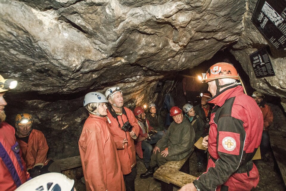 Eine Gruppe von Menschen in einem Höhlenraum hört einem Führer zu. Alle tragen Helme und sind in Schutzkleidung.