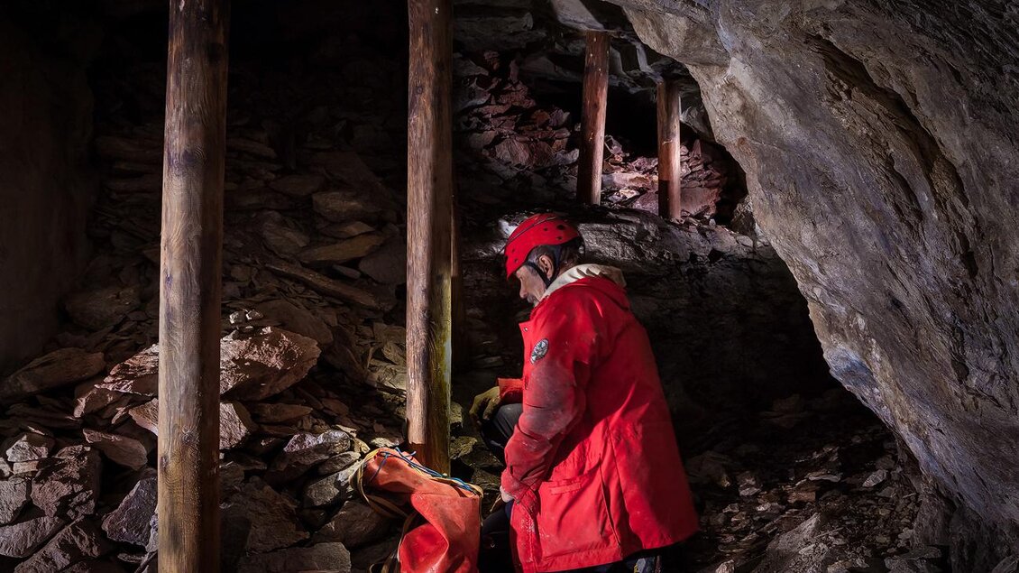 Ein Mensch in einem roten Anzug arbeitet in einer Höhle. Die Umgebung besteht aus Felsen und Holzstützen.