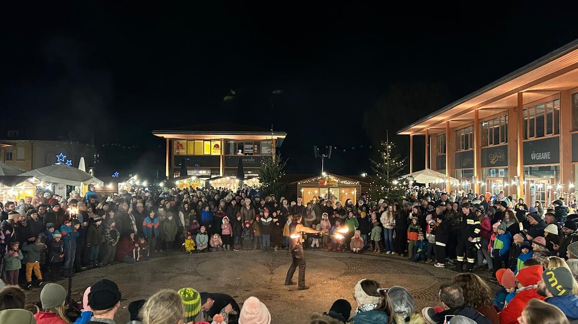 Eine große Menschenmenge versammelt sich bei Nacht, um einer Feuershow zuzusehen. Im Hintergrund sind festlich beleuchtete Stände zu sehen. | © Marktgemeinde Gratwein-Straßengel