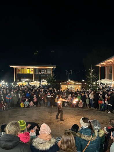 Eine große Menschenmenge versammelt sich bei Nacht, um einer Feuershow zuzusehen. Im Hintergrund sind festlich beleuchtete Stände zu sehen. | © Marktgemeinde Gratwein-Straßengel