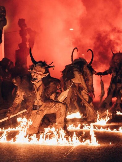 Eine Gruppe von verkleideten Figuren zieht durch eine Straße, umgeben von Feuer und Rauch. Die Atmosphäre ist festlich und zugleich bedrohlich. | © Südsteirische Teufel