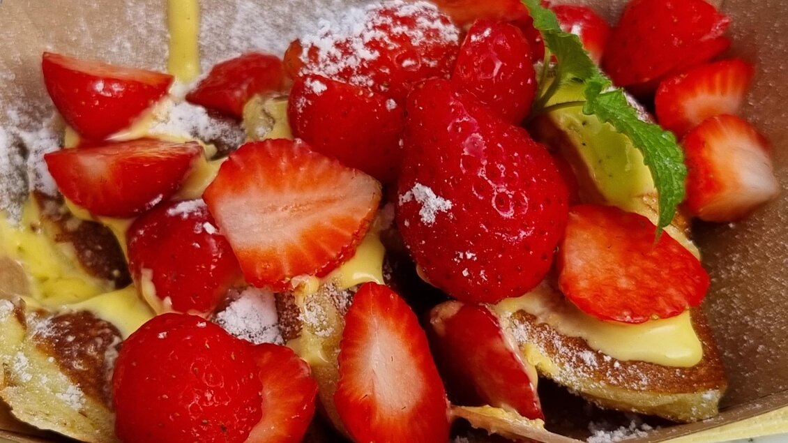 Ein Schälchen mit frischen Erdbeeren, garniert mit Puderzucker und einer cremigen Sauce. Das Gericht sieht erfrischend und einladend aus. | © Grill Thomas