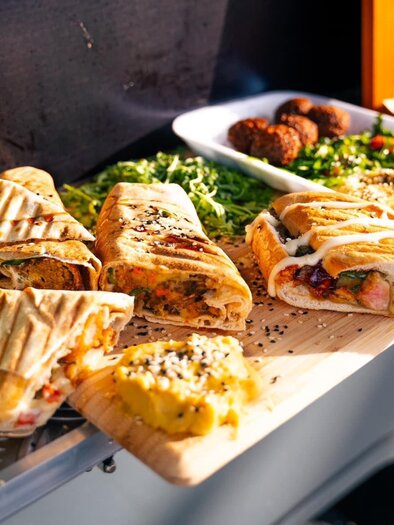 A food truck with various delicious dishes.  
There are stuffed sandwiches, fresh salads, and snacks presented on a table. | © Oststeiermark Tourismus