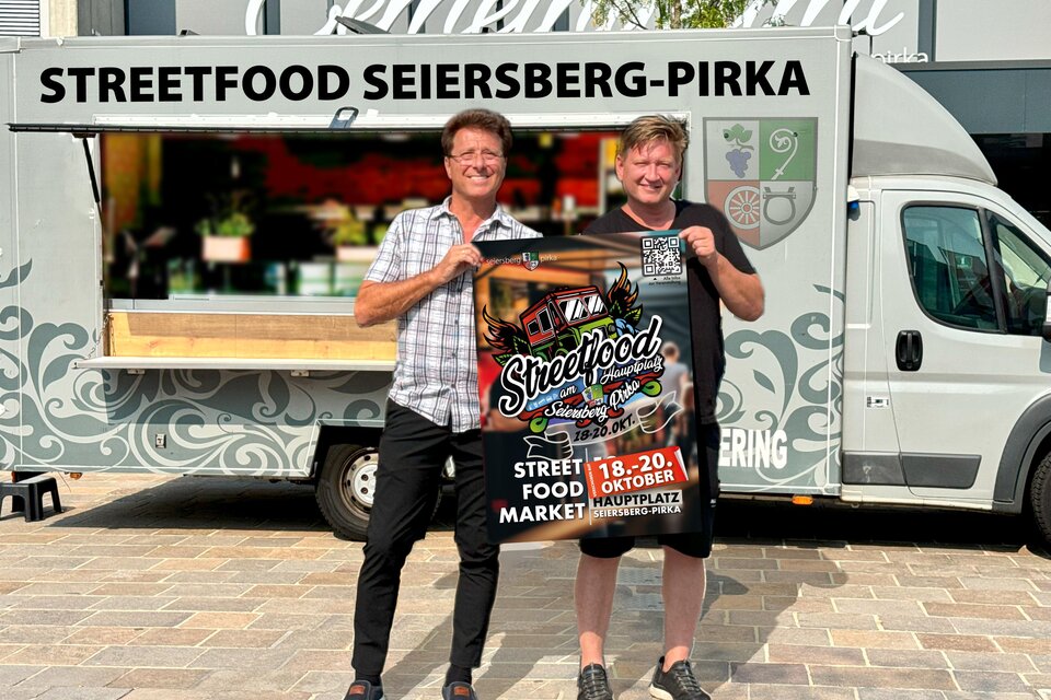 Zwei Männer stehen vor einem Food Truck und halten ein Plakat für das Streetfood-Event in Seiersberg-Pirka. Im Hintergrund ist der Food Truck mit dem Schriftzug "Streetfood Seiersberg-Pirka" zu sehen. | © Gemeinde Seiersberg-Pirka
