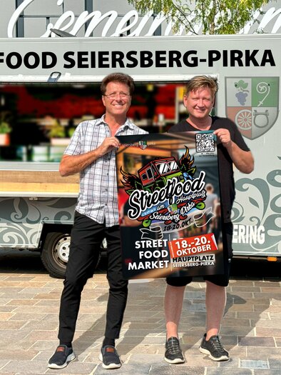 Zwei Männer stehen vor einem Food Truck und halten ein Plakat für das Streetfood-Event in Seiersberg-Pirka. Im Hintergrund ist der Food Truck mit dem Schriftzug "Streetfood Seiersberg-Pirka" zu sehen. | © Gemeinde Seiersberg-Pirka