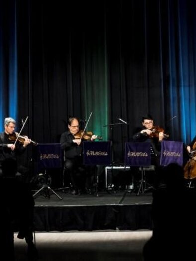 Eine Musikgruppe steht auf der Bühne und spielt verschiedene Instrumente. Im Hintergrund leuchten bunte Lichter. | © Kuturforum Bad Radkersburg