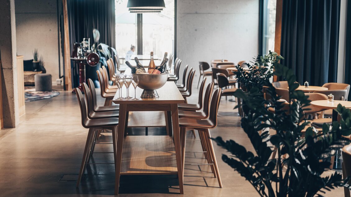 Ein modernes Restaurant mit einem langen Holztisch und Holzstühlen. Große Fenster sorgen für viel Tageslicht und Pflanzen verleihen eine einladende Atmosphäre. | © Ian Ehm