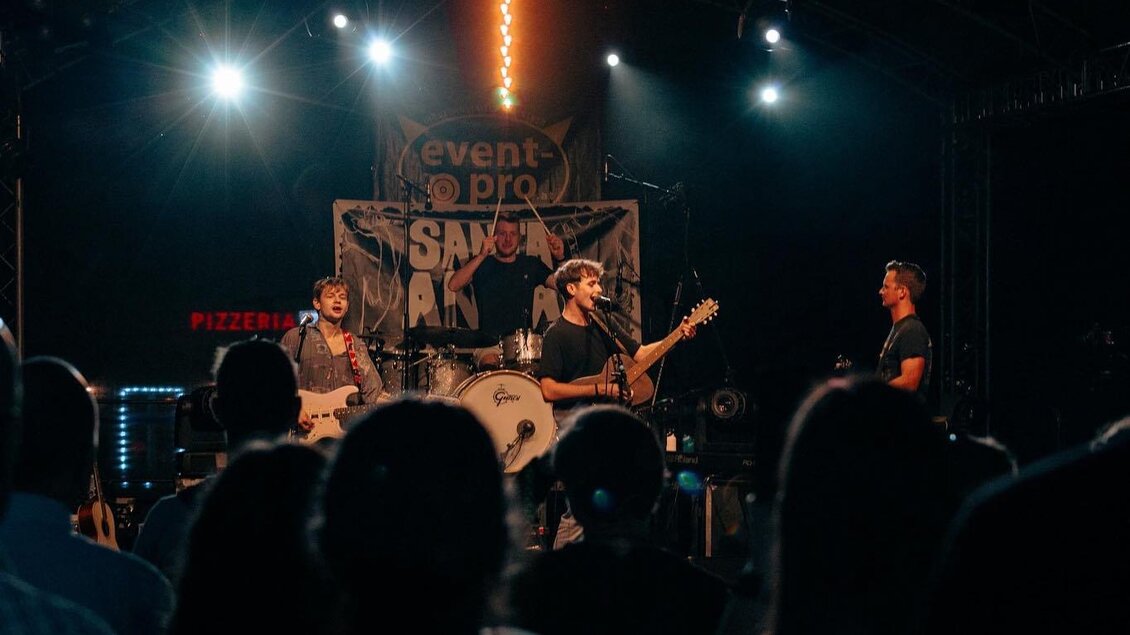 Eine Band spielt live auf einer Bühne im Scheinwerferlicht. Das Publikum schaut begeistert zu. | © Santa Anna