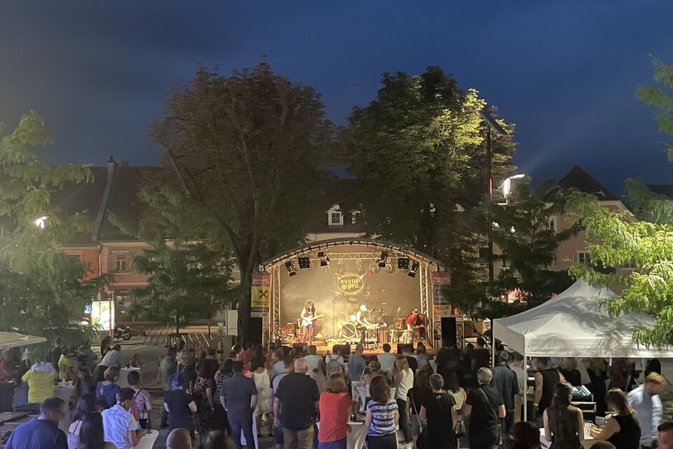 Ein Konzert im Freien bei Nacht mit einer großen Menschenmenge. Die Bühne ist gut beleuchtet und es sind mehrere Musiker zu sehen.