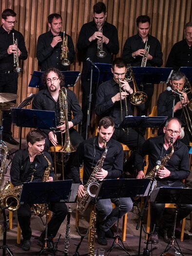 Eine Jazzband spielt auf einer Bühne. Die Musiker sind in schwarzen Outfits gekleidet und spielen verschiedene Instrumente. | © Big Band Hartberg