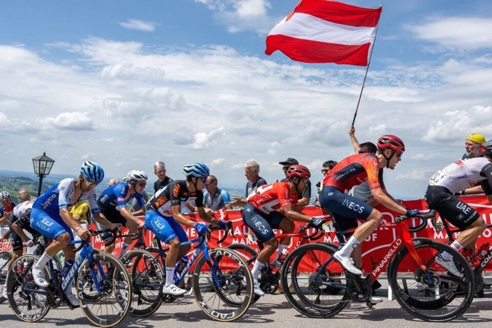 Eine Gruppe Radfahrer fährt auf einer Rennstrecke. Im Hintergrund schwenkt ein Zuschauer eine rot-weiß-rote Flagge. | © EXPA