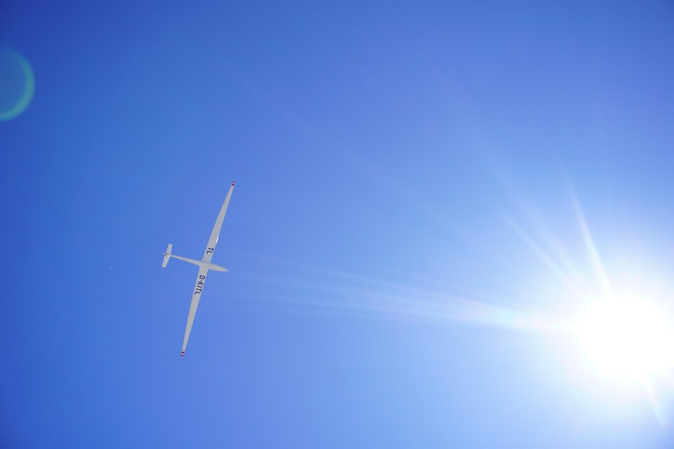 Ein Segelflugzeug fliegt hoch am klaren blauen Himmel. Die Sonne strahlt hell im Bild. | © TV Hochsteiermark
