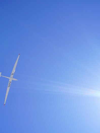 Ein Segelflugzeug fliegt hoch am klaren blauen Himmel. Die Sonne strahlt hell im Bild. | © TV Hochsteiermark