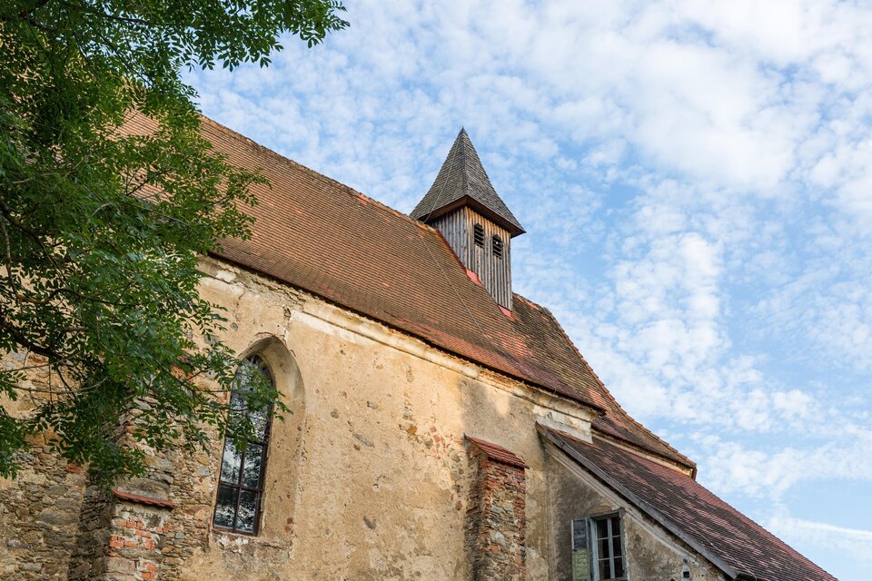 Eine alte Kirche mit einem spitzen Dach und großen Fenstern. Der Himmel ist blau und mit einigen Wolken bedeckt. | © fotodesign by Marcus Auer