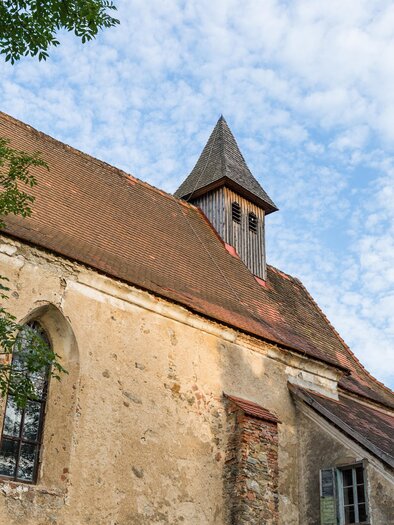 Eine alte Kirche mit einem spitzen Dach und großen Fenstern. Der Himmel ist blau und mit einigen Wolken bedeckt. | © fotodesign by Marcus Auer