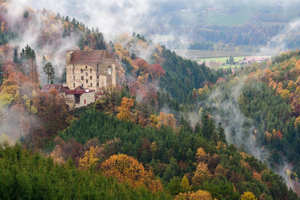 Eine alte Burg liegt malerisch in einem nebligen Wald. Bunte Herbstlaub umgibt das Bühnenbild und schafft eine mystische Atmosphäre. | © Ewald Neffe_Oststeiermark