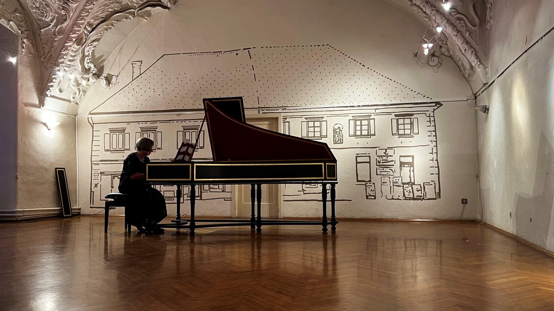 Eine Person spielt ein Cembalo in einem eleganten Raum mit hohen Decken. Die Wände sind mit einem skizzierten Haus dekoriert. | © Tage der Alten Musik
