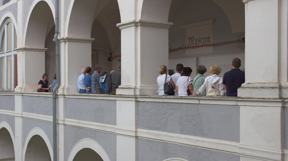Eine Gruppe von Menschen steht auf einem Balkon mit Bögen. Sie scheinen ein Museum zu besuchen. | © Tage der alten Musik