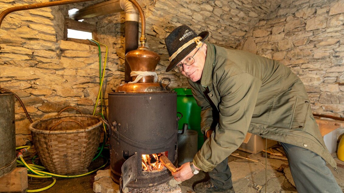 Ein Mann facht ein Feuer in einem traditionellen Holzofen an. Im Hintergrund sieht man Steinwände und einige Utensilien. | © Region Graz - Harry Schiffer