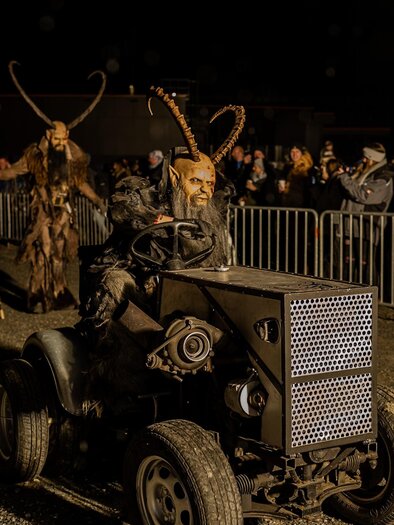 A creative parade with people in costumes and masks riding on a tractor. In the background, many spectators can be seen. | © Tv Murau