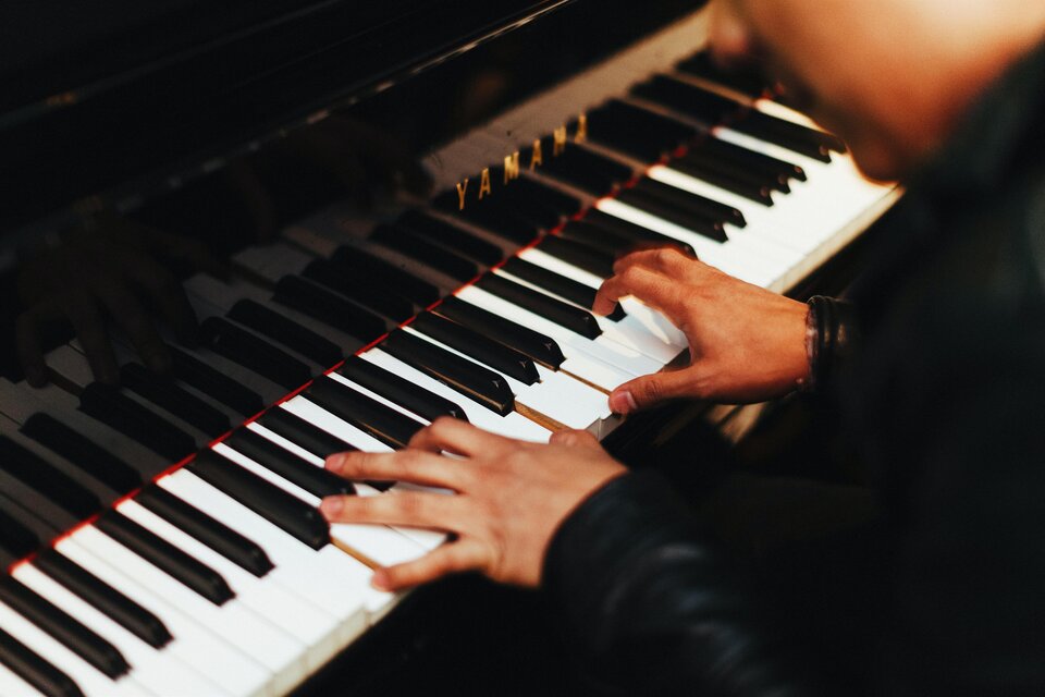 Ein Musiker spielt auf einem Klavier mit schwarzen und weißen Tasten. Die Hände sind in Aktion, während die Musik erklingt.