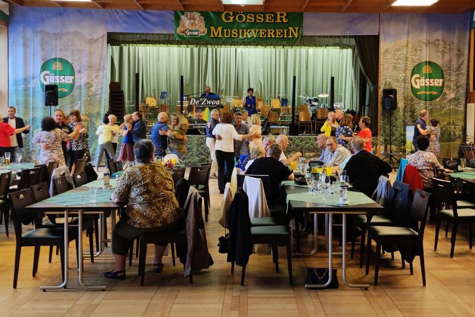 Menschen tanzen und haben Spaß in einem festlichen Saal mit Tischen. Im Hintergrund ist eine Band auf der Bühne sichtbar. | © Referat Soziales, Familien & Frauen