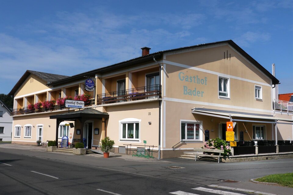 Ein gemütliches Gasthaus mit gelber Fassade und Balkon. Es liegt an einer Straße und ist von einem kleinen Garten umgeben. | © Gasthof Bader