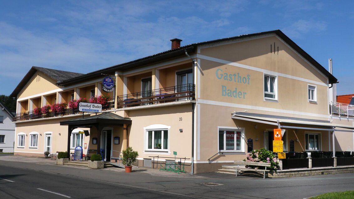 Ein gemütliches Gasthaus mit gelber Fassade und Balkon. Es liegt an einer Straße und ist von einem kleinen Garten umgeben. | © Gasthof Bader