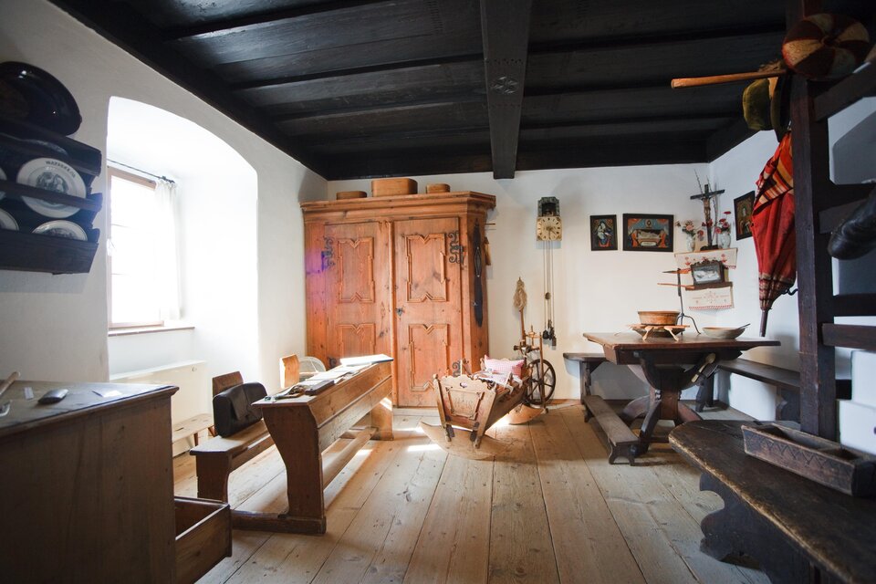 Ein traditionelles Zimmer mit Holzdecke und historischen Möbeln. Ein großer Holzschrank und ein Tisch sind im Raum vorhanden. | © Fred Lindmoser
