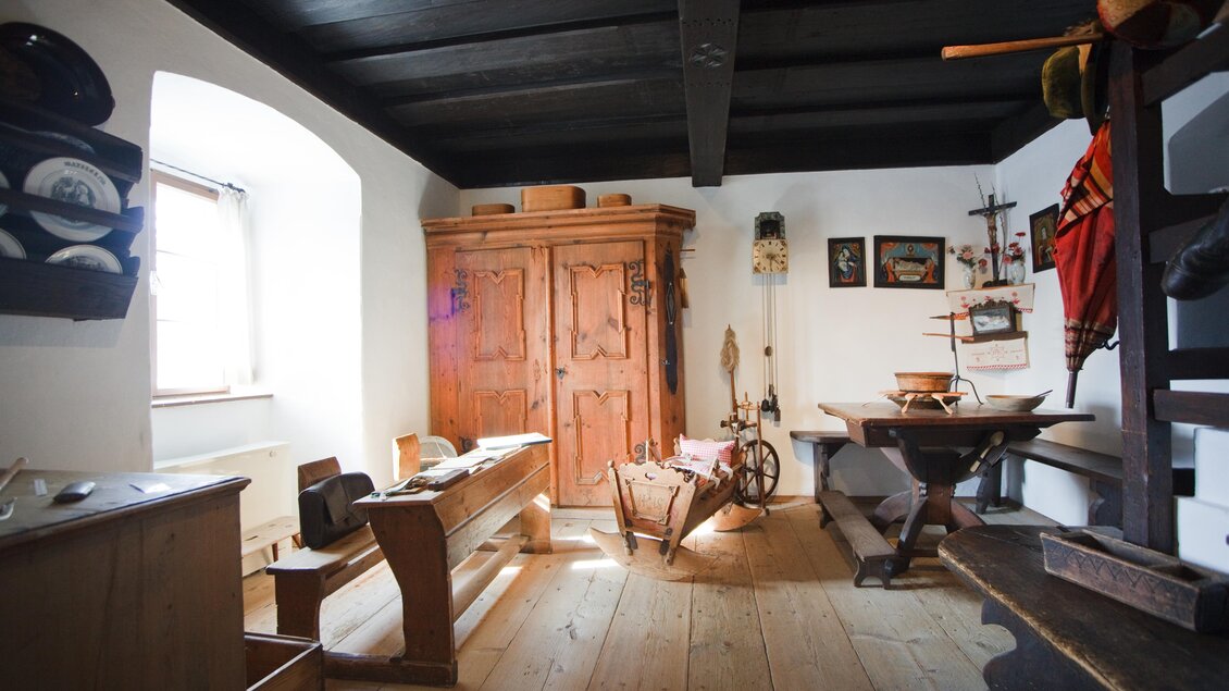 Ein traditionelles Zimmer mit Holzdecke und historischen Möbeln. Ein großer Holzschrank und ein Tisch sind im Raum vorhanden. | © Fred Lindmoser