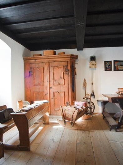 Ein traditionelles Zimmer mit Holzdecke und historischen Möbeln. Ein großer Holzschrank und ein Tisch sind im Raum vorhanden. | © Fred Lindmoser
