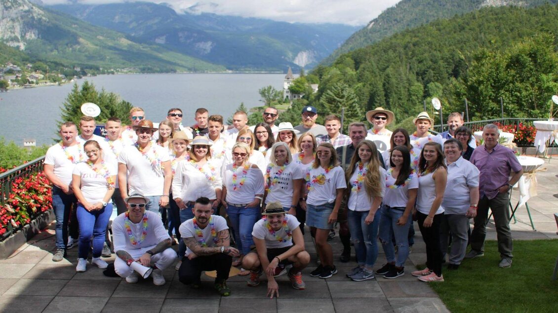 Das MONDI Team beim Terrassenfest in Grundlsee steht lächelnd auf der Seeterrasse zusammen. Im Hintergrund ist der malerische Grundlsee und die Berge in der Landschaft des Ausseerlandes zu sehen. | © Mondi Grundlse