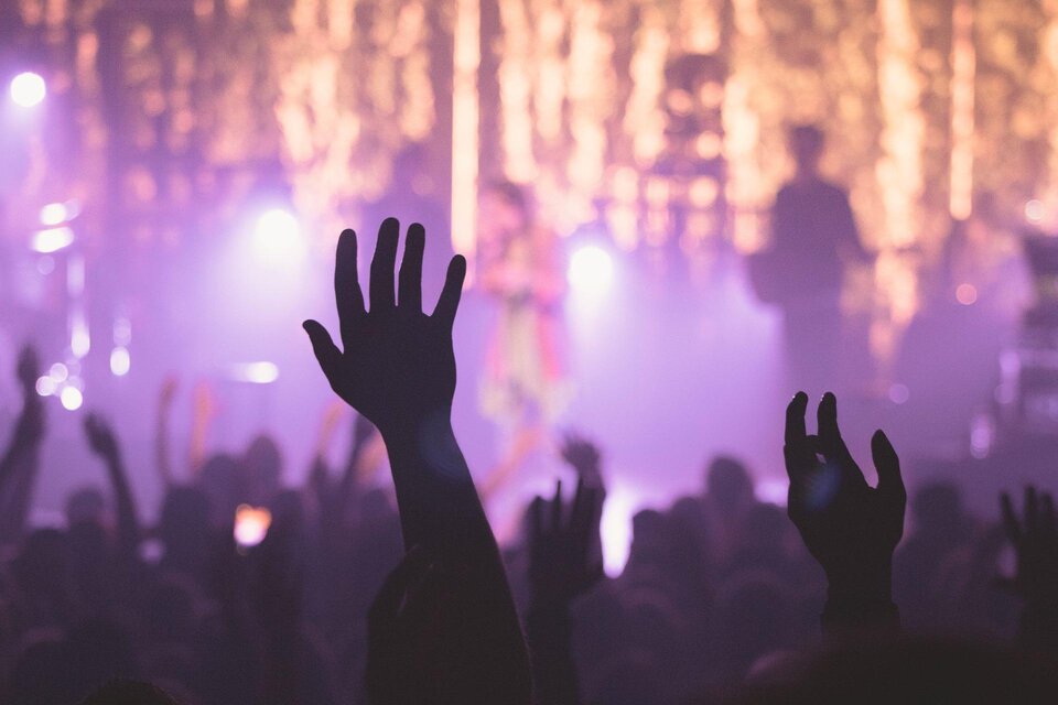 Eine begeisterte Menschenmenge hebt ihre Hände bei einem Live-Konzert. Die Bühne ist von bunten Lichtern und einem festlichen Ambiente umgeben. | © Pixabay