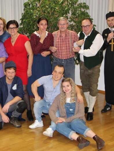 A group of twelve people stands together in a room. Some of them are wearing various costumes, including medical and historical attire. | © Theaterverein "Wir theatern wieder"