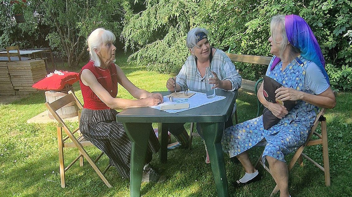 Drei Frauen sitzen entspannt im Garten an einem Tisch. Sie scheinen ein Spiel oder eine Aktivität zu genießen. | © TRUNK-Elfi Greiner