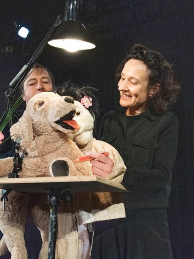 Zwei Frauen stehen auf einer Bühne und bedienen Puppen. Eine der Puppen hält eine Blume und die Atmosphäre ist kreativ und freundlich. | © Peter Pfister