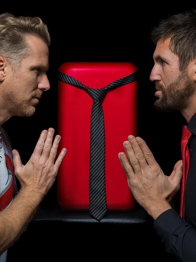 Andreas Ortner und Markus Perner stehen sich auf einer Bühne oder im Studio gegenüber, zwischen ihnen ein roter Kühlschrank mit Krawatte – humorvolle Inszenierung des Kabarett- und Comedy-Duos Kühlschrank23, kreative Unterhaltung und kulturelle Vielfalt in der Stadthalle Fürstenfeld. | © Richard Weiß