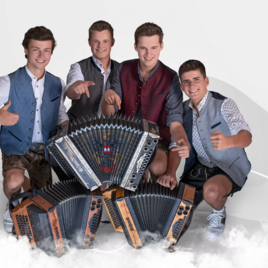 Four young men pose enthusiastically around several accordions. They wear traditional clothing and display cheerful gestures. | © Brennholz_FF Obertiefenbach