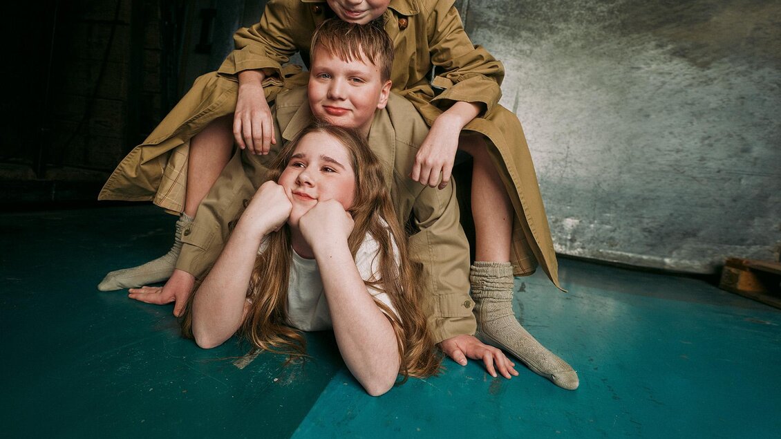 Drei Kinder posieren spielerisch auf dem Boden. Sie tragen einfache Kleidung und haben fröhliche Gesichtsausdrücke. | © -marko-mestrovic.