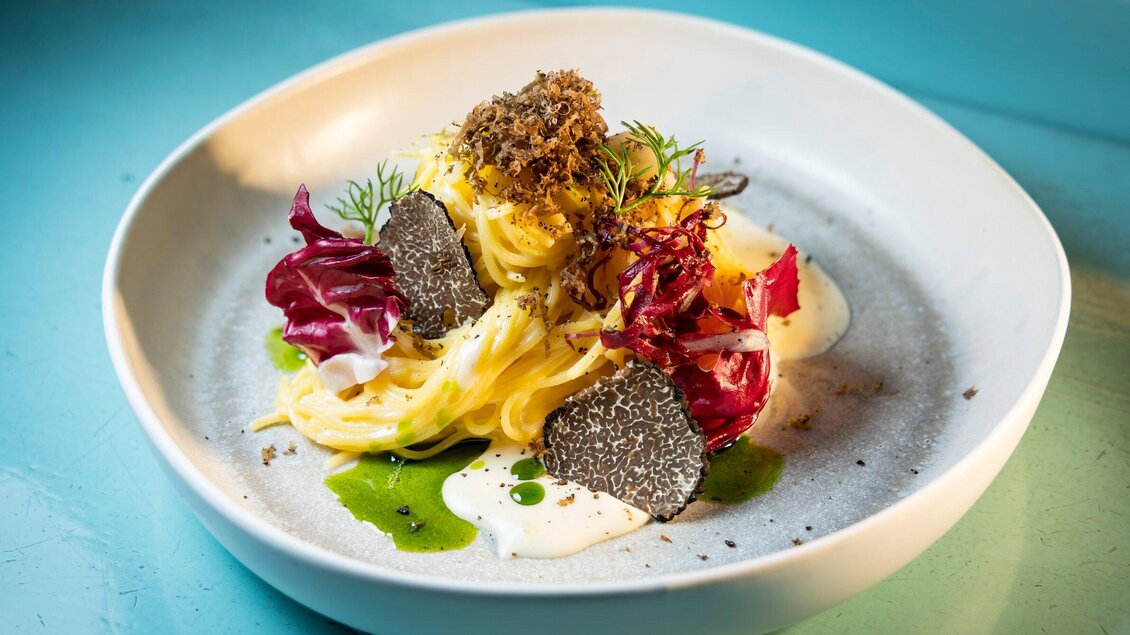 Ein eleganter Teller mit Pasta, garniert mit Radicchio, Kräutern und schwarzem Trüffel. Die Anrichtung ist ansprechend und farbenfroh, mit einer cremigen Sauce. | © Graz Tourismus - Werner Krug