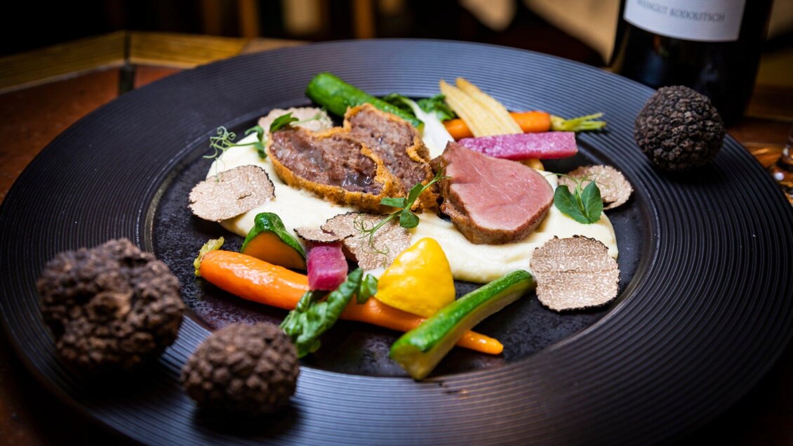 Ein stilvolles Gericht mit zartem Fleisch, umgeben von buntem Gemüse und Trüffeln. Ansprechend angerichtet auf einem schwarzen Teller. | © Graz Tourismus - Werner Krug